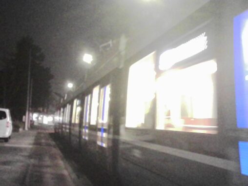 A foggy nighttime street as a passing streetcar creates bright, elongated bands of light, diffusing through the mist and introducing motion blur along the tracks and pavement.