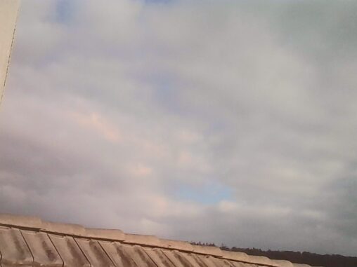 Cloudy sky above rooftops with soft light and small patches of blue breaking through after rain.