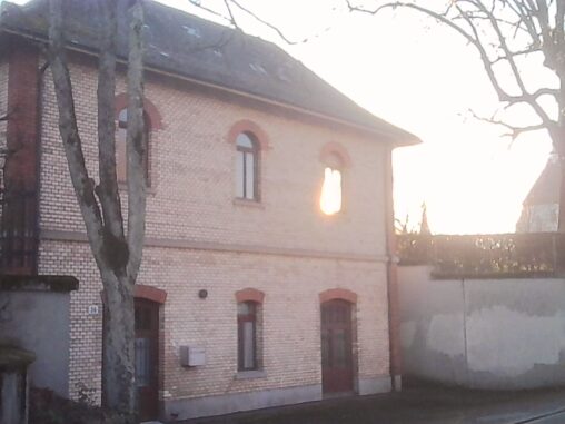 Low winter sun shining through a window of a brick building, illuminating the interior while bare tree branches frame the scene.