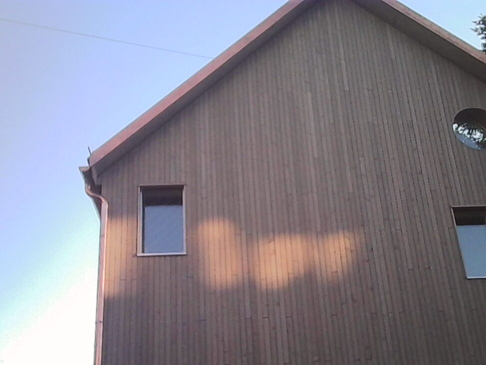 Sunset reflection forming a horizontal stripe of warm light across the wooden facade of a house beneath a clear evening sky.