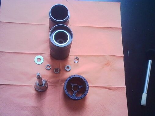 Disassembled manual coffee grinder parts arranged neatly on an orange cloth, including burrs, shaft, washers, and housing components.