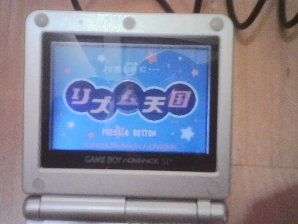 Close-up of a silver Game Boy Advance SP showing a colorful retro game screen, photographed in soft indoor light.