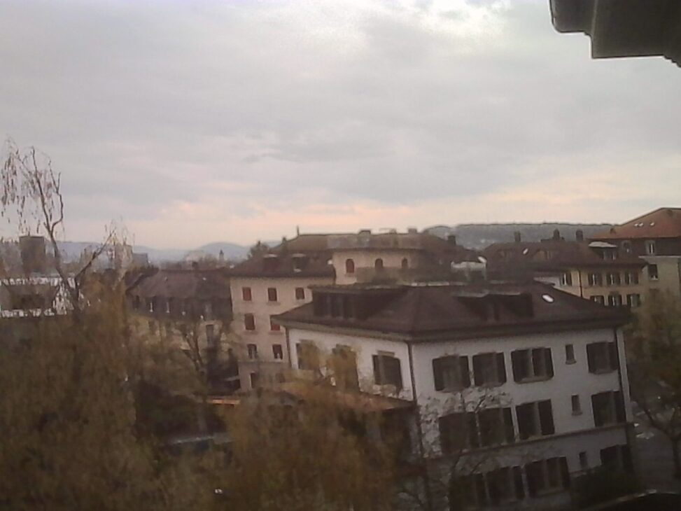Hazy view from USZ over Zurich towards the Limmat valley hill, barely emerging through a grey sky.