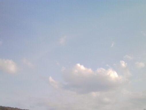 Soft clouds drifting across a pale blue sky, with sunlight breaking through.