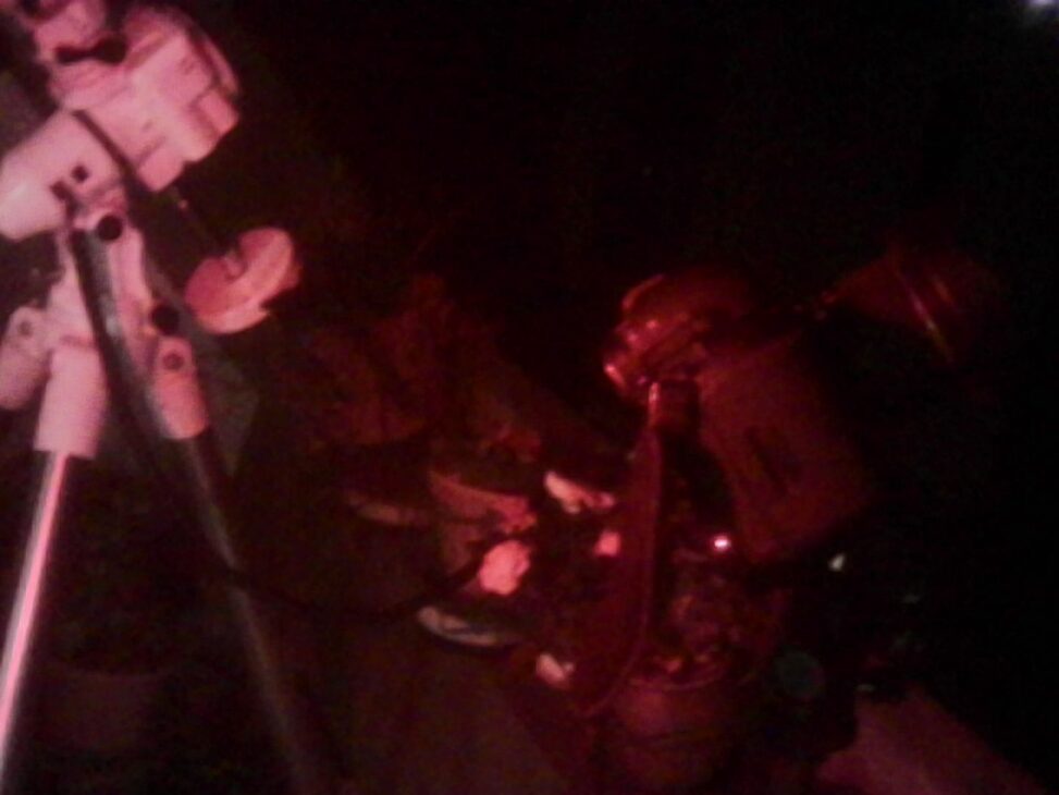 elescope and camera setup under red light at night, with equipment arranged on a balcony for a Lyrid meteor shower session in an urban sky.