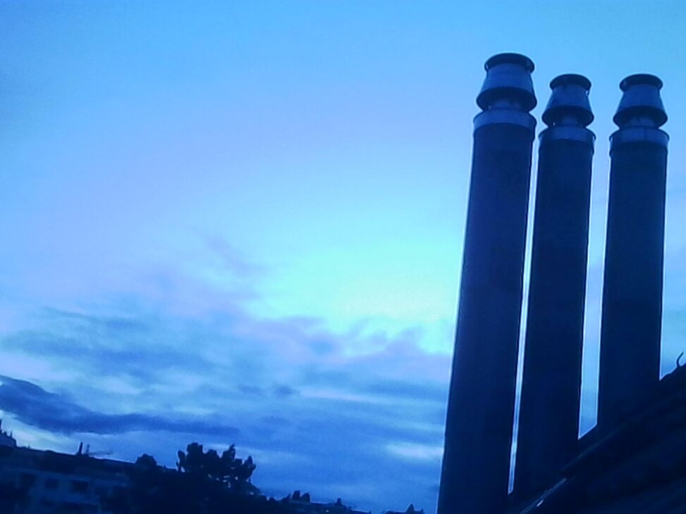 Three chimneys silhouetted against a blue evening sky with layered clouds