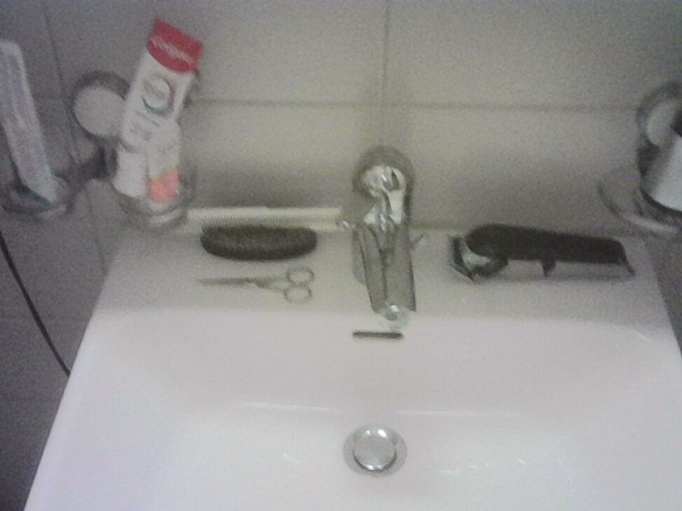 Bathroom sink with a beard trimmer, grooming scissors, hairbrush, toothpaste, and other toiletries neatly arranged after a simple grooming routine.