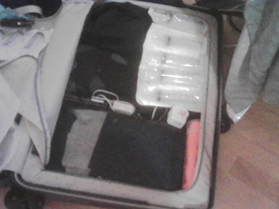 An open suitcase being packed for a trip, with clothing, packing cubes, medical supplies and small electronic devices tightly arranged inside.