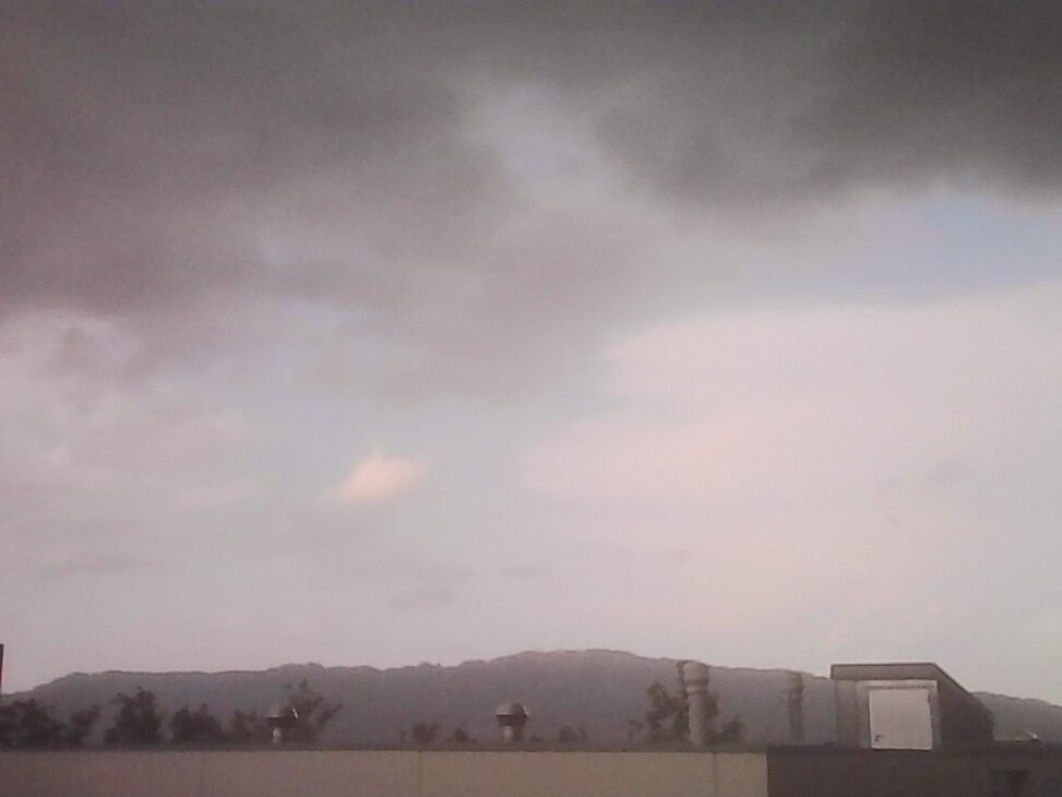 Dark storm clouds passing over Zurich, with the silhouette of Uetliberg stretching across the horizon beneath a pale, rain-filled sky.